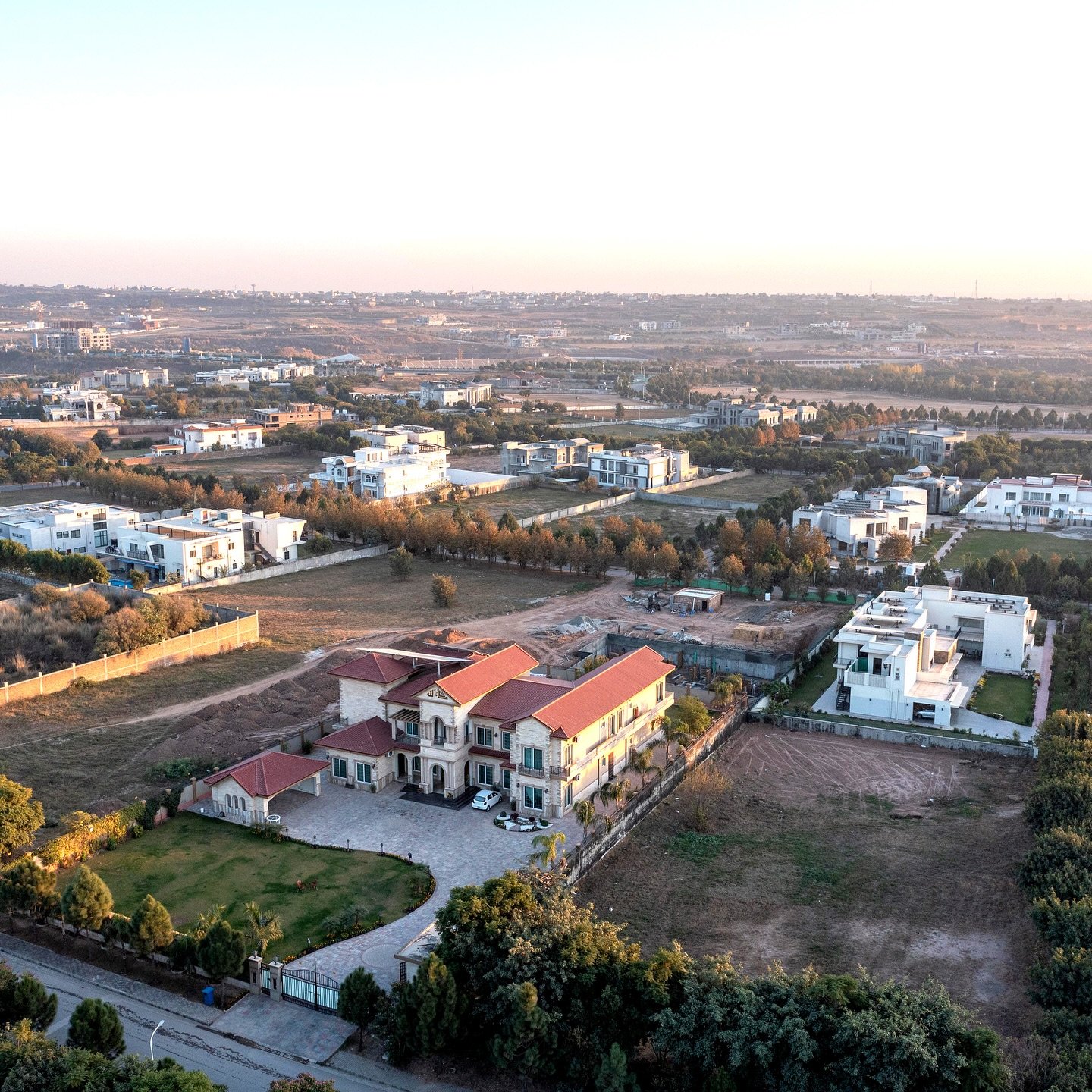 Aerial view at golden hour over farmhouses, tree lines and open plots in Gulberg Greens, Islamabad